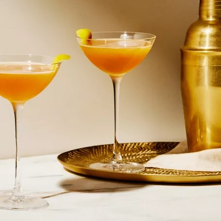 Cognac cocktails made with Courvoisier French Cognac poured into Nick and Nora glasses on a gold tray and marble table next to a gold cocktail shaker.