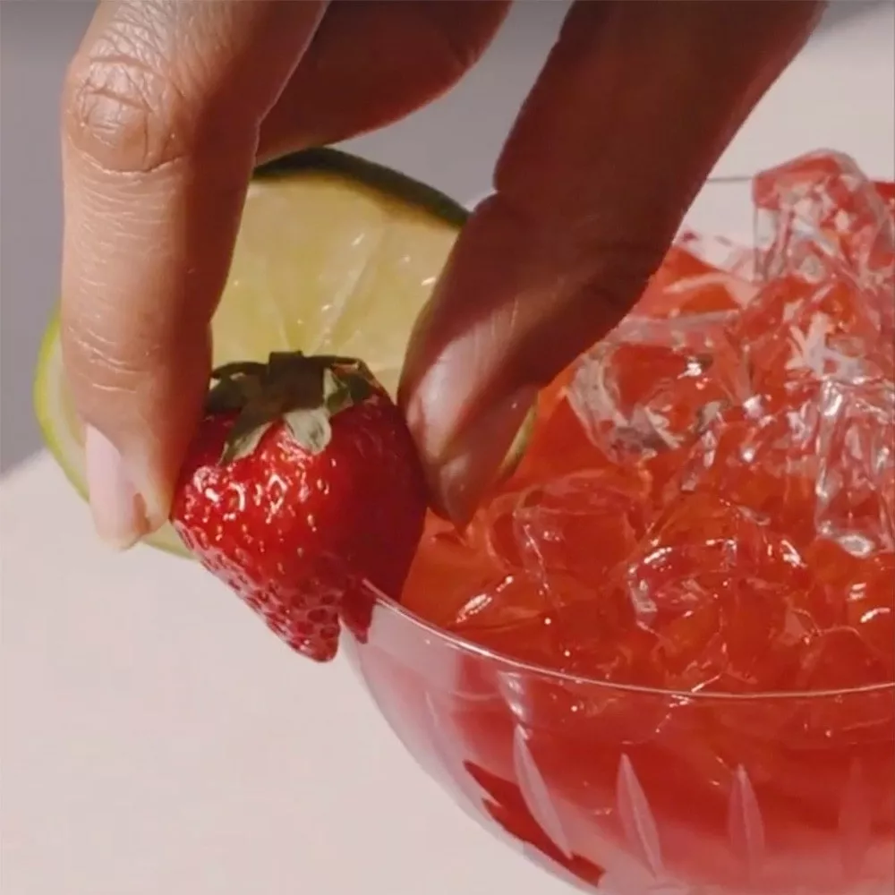 Garnishing a cocktail with cognac with a strawberry and lime