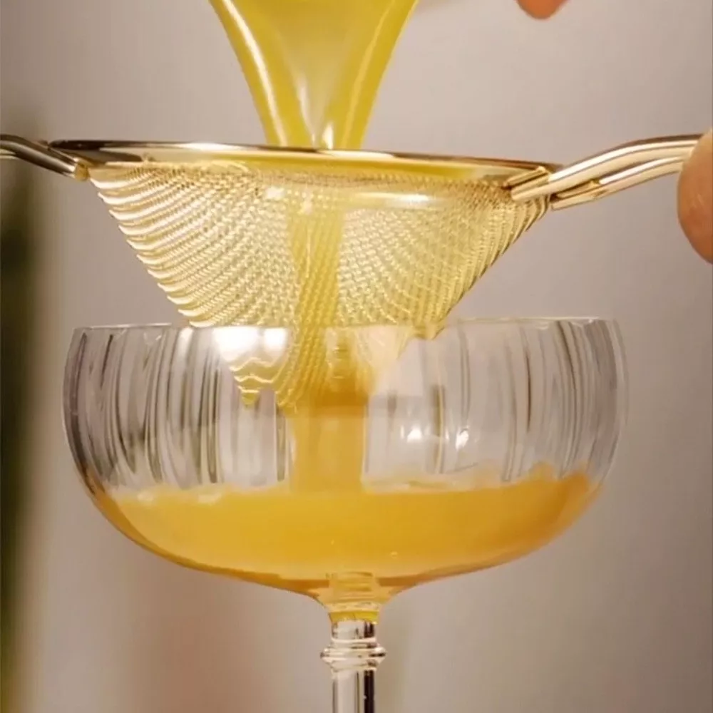 Straining a cognac-based cocktail into a glass